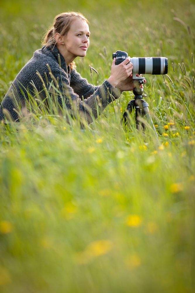 Pretty young woman with a DSLR camera outdoors, using a tripod, taking pictures