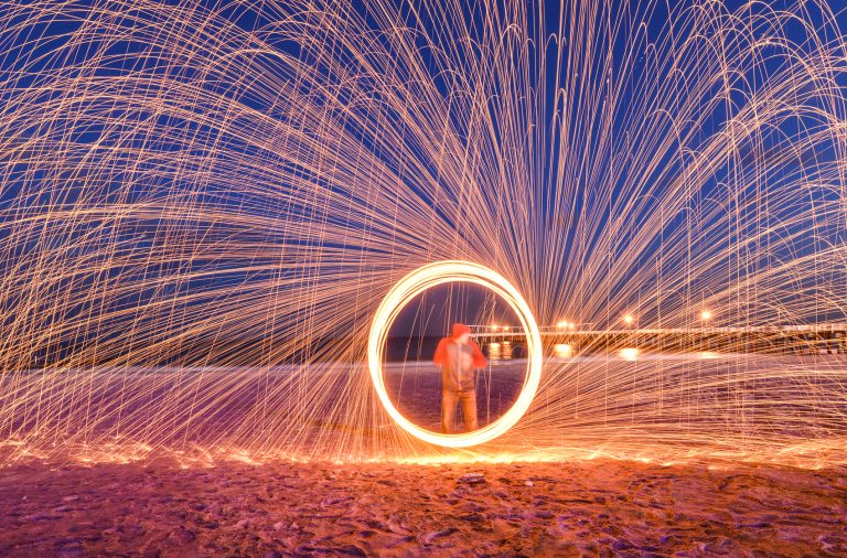 man doing steel wool photography on a beach